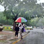 A man and his child take shelter under an umbrella to stay dry during the monsoon downpour in the Federal Capital