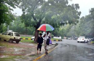 A man and his child take shelter under an umbrella to stay dry during the monsoon downpour in the Federal Capital