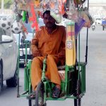 A disabled street vendor pedals his tricycle, loaded with colorful plastic toys, as he navigates through city streets in search of customers