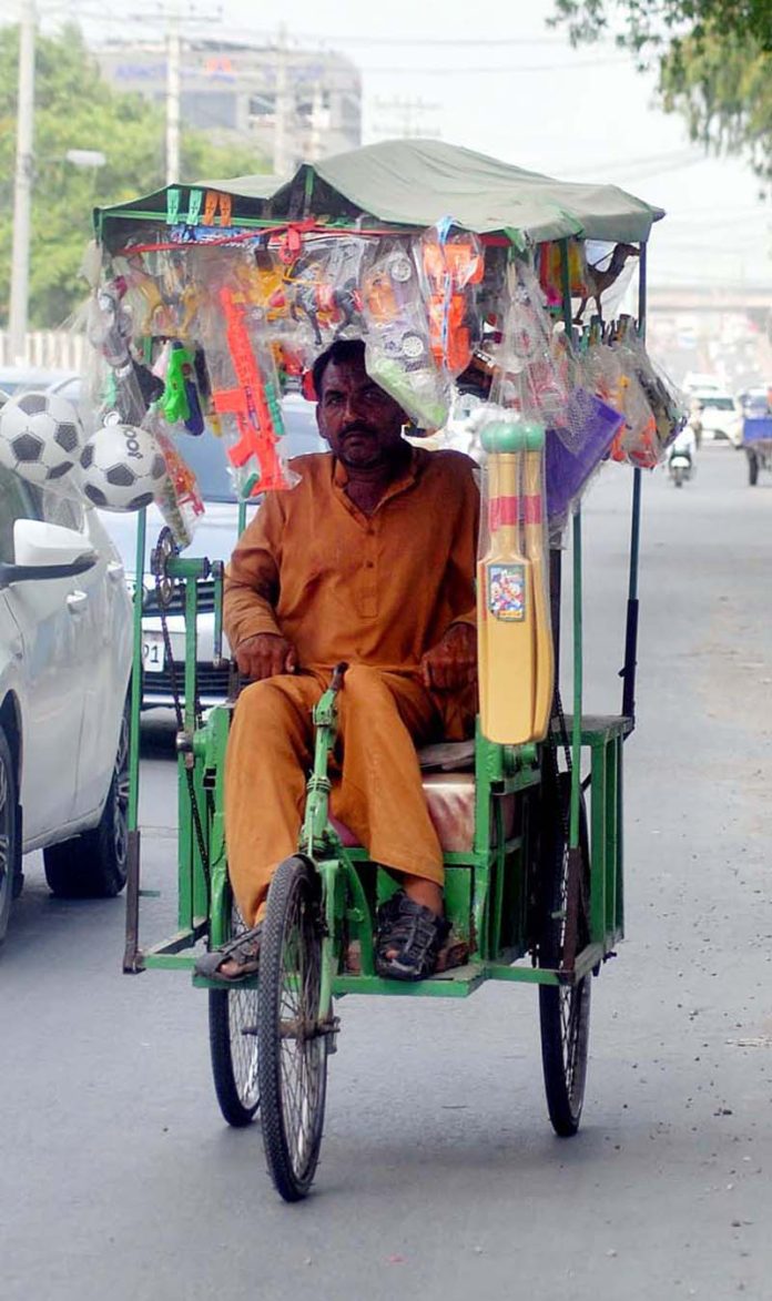 A disabled street vendor pedals his tricycle, loaded with colorful plastic toys, as he navigates through city streets in search of customers