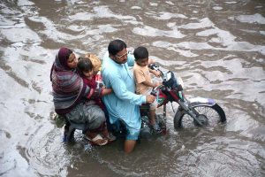 A family on a motorcycle struggles to make its way through rainwater flooding Jhumra Road near Nishatabad Bridge after a heavy downpour, causing traffic disruption and public inconvenience