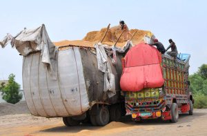 Labourers are busy transferring a large quantity of wheat husk from an overfilled trailer into a delivery truck at a roadside loading point in the outskirts of the city.