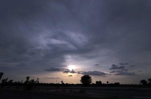 The setting sun peeks through thick clouds, creating a mesmerizing scene like a painting brushed across the sky after a mildly humid day in the city.