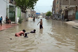 Children enjoy bathe in rainwater accumulated on Makki Shah Road, which was submerged following heavy rainfall