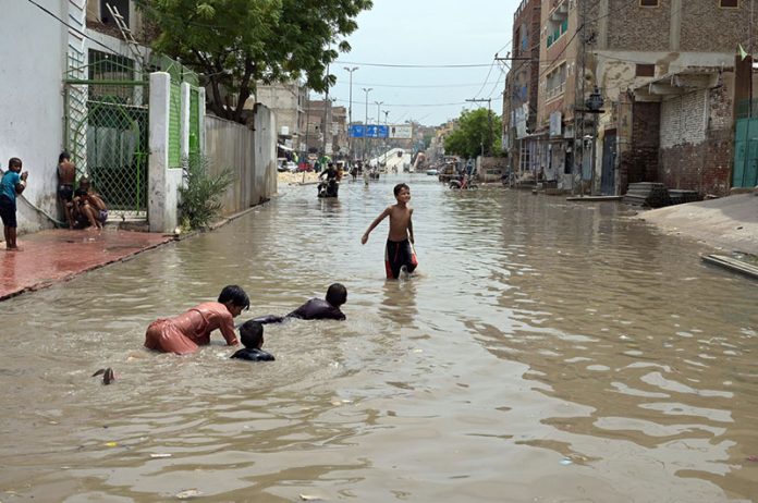 Children enjoy bathe in rainwater accumulated on Makki Shah Road, which was submerged following heavy rainfall