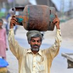A man carries an empty LPG cylinder to a local shop for refilling in a suburban neighborhood
