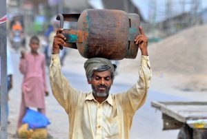 A man carries an empty LPG cylinder to a local shop for refilling in a suburban neighborhood
