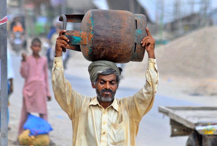 A man carries an empty LPG cylinder to a local shop for refilling in a suburban neighborhood