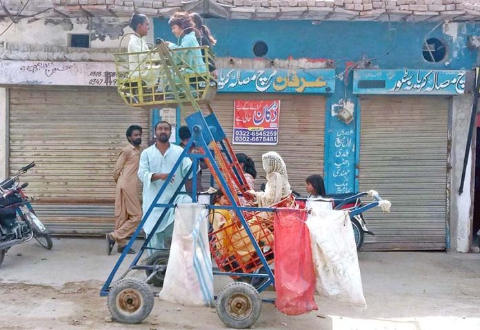 Children enjoy riding a mini Sky Wheel on the side of the road in a neighborhood of Bahawalpur city