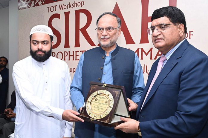 Program host Qamarul Haq presents a shield to Federal Minister for Planning, Development and Special Initiatives, Ahsan Iqbal, during the Seerah Workshop at Seerah Center