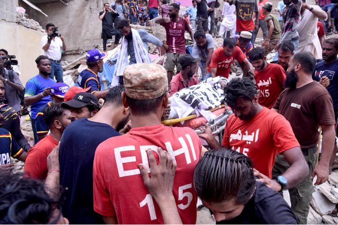 A body is being retrieved from the debris of a collapsed residential building in Baghdadi, Lyari. Rescue workers continue their efforts amid scenes of devastation and despair