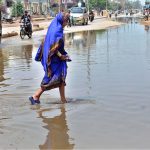 A woman walks through accumulated sewage water on a road in Latifabad, disrupting smooth traffic flow and the daily routine of local residents