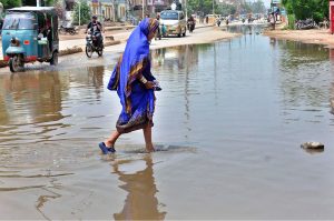 A woman walks through accumulated sewage water on a road in Latifabad, disrupting smooth traffic flow and the daily routine of local residents