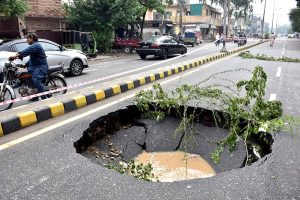 A large sinkhole filled with rainwater appears on a busy road near Wahdat Colony following recent downpours, prompting authorities to cordon off the area for public safety.