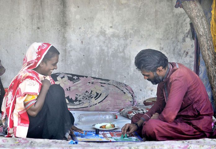 A gypsy couple enjoys a game of Ludo on a roadside footpath, turning leisure time into a simple moment of joy