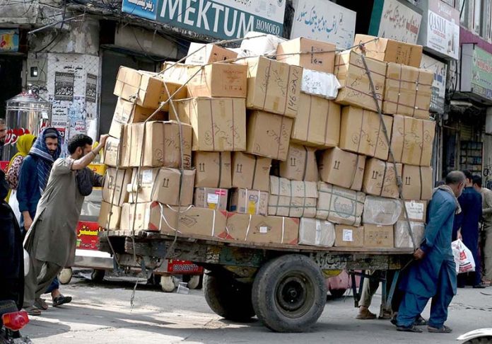 A daily-wage laborer pulls an overloaded cart of goods for transport and delivery to the market in Raja Bazaar, one of the busiest areas in the twin cities