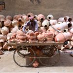 An elderly man displays clay pots on his hand cart to attract customers at Kumhar Para, showcasing traditional craftsmanship
