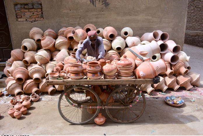 An elderly man displays clay pots on his hand cart to attract customers at Kumhar Para, showcasing traditional craftsmanship