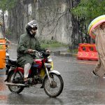 A motorcyclist and a pedestrian shield themselves from heavy rain during the second spell of the monsoon in the provincial capital