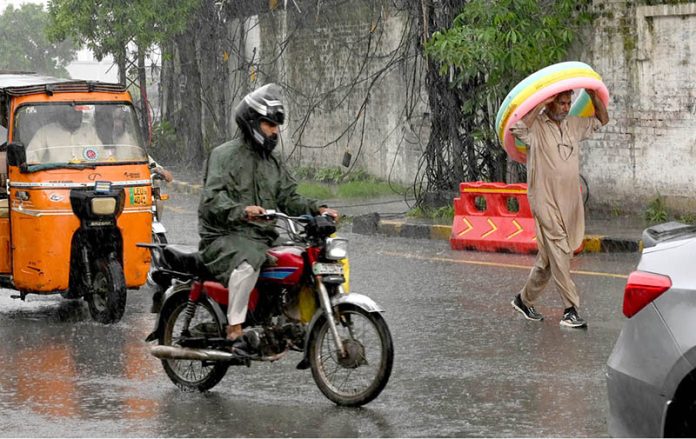 A motorcyclist and a pedestrian shield themselves from heavy rain during the second spell of the monsoon in the provincial capital