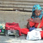 A woman uses a hand fan to cool her child while selling colorful chicks during the scorching heat in Latifabad