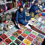 A street vendor arranges colorful gemstones and beautiful rings to attract customers at his roadside setup in a local market