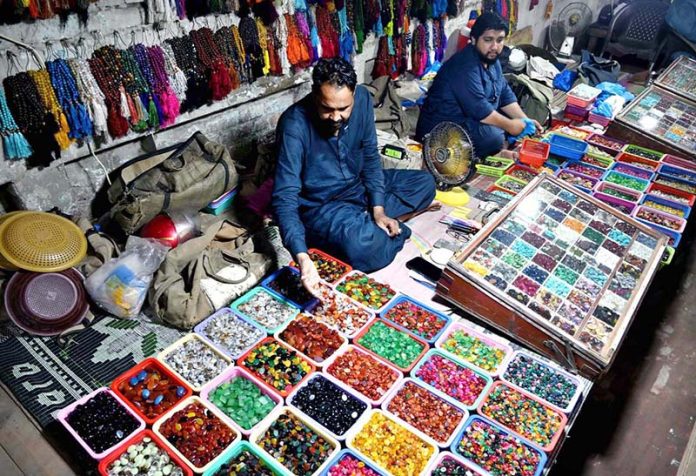 A street vendor arranges colorful gemstones and beautiful rings to attract customers at his roadside setup in a local market