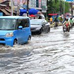 Vehicles and motorbikes pass through a flooded road after torrential monsoon rain disrupted daily life in the city