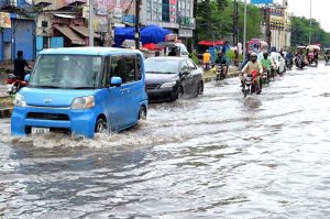 Vehicles and motorbikes pass through a flooded road after torrential monsoon rain disrupted daily life in the city