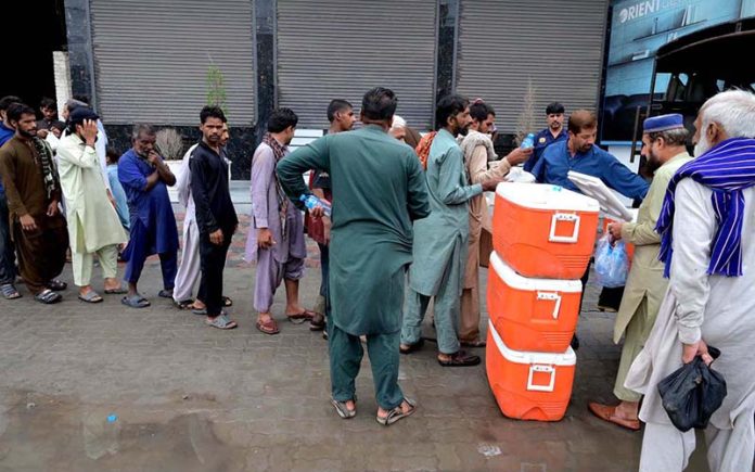People queue for their turn to receive free food as volunteers distribute free food among people in Kotli Bahram