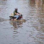 A motorcyclist passing through accumulated water on the road after heavy rain in the Provincial Capital