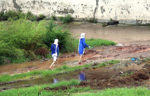 Students on the way while passing through mud at Tarlai after rainfall in the Federal Capital.