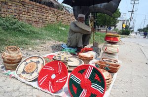 An elderly vendor waits for customers to sell household items at his roadside setup.