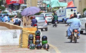 A vendor is displaying helmets and caps on handcart on footpath under a 'No Parking' sign along Murree Road.