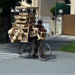 A vendor displays and sells wooden benches and handmade nests on his bicycle to attract customers along a road in the federal capital