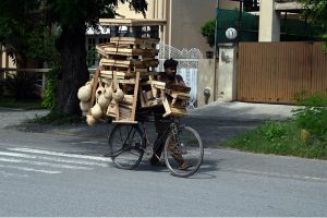 A vendor displays and sells wooden benches and handmade nests on his bicycle to attract customers along a road in the federal capital