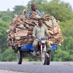 A motorcycle cart carrying a large load of empty cement bags heads to collection points around the city, where workers collect and resell recyclable materials for their livelihood