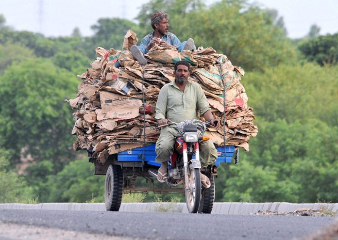 A motorcycle cart carrying a large load of empty cement bags heads to collection points around the city, where workers collect and resell recyclable materials for their livelihood