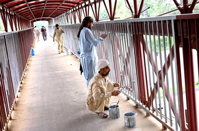 Workers busy painting a pedestrian bridge at Zero Point in the Federal Capital