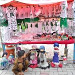 A young vendor arranging and displaying national flag color children dresses and other items related to Independence Day celebrations at his roadside setup.
