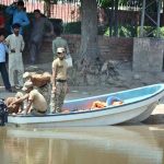 Rescue workers repair a lifesaving boat before launching operations as the swollen River Chenab carries heavy floodwater through Chiniot district.