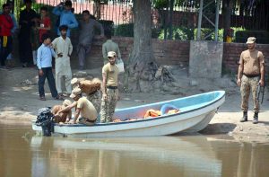 Rescue workers repair a lifesaving boat before launching operations as the swollen River Chenab carries heavy floodwater through Chiniot district.