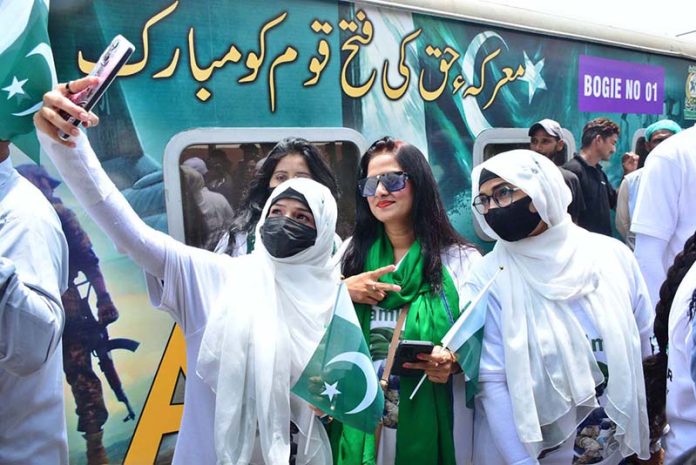 Women passengers take a selfie with a cell phone in front of the Thar Desert Safari Azadi Train at the railway station, traveling from Karachi to Khokhrapar as part of the 78th Independence Day and 'Marka-e-Haq' celebrations