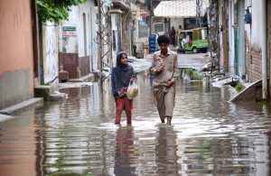 People passing through rainwater accumulated in the street after heavy rain in Provincial Capital.