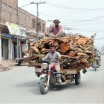 A person sitting on chopped wood loaded on tricycle loader on the way
