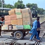 Labourers are pushing and pulling hand cart heavily loaded with luggage as they cross railway tracks near Railway Station