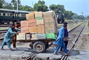 Labourers are pushing and pulling hand cart heavily loaded with luggage as they cross railway tracks near Railway Station