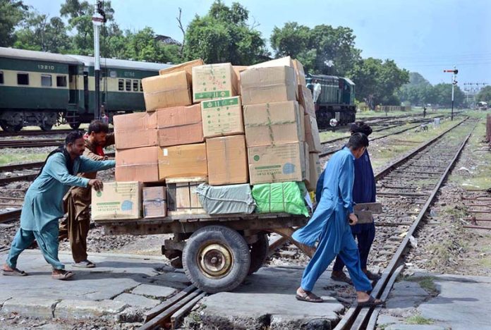 Labourers are pushing and pulling hand cart heavily loaded with luggage as they cross railway tracks near Railway Station