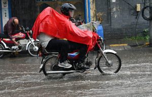 A motorcyclist balances his ride with an umbrella in hand to shield himself from heavy rainfall while passing through the city.