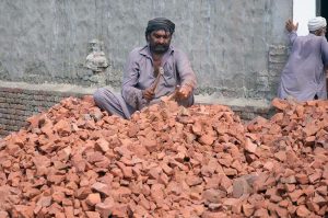 A Labourer busy in crushing bricks into pieces during construction work.